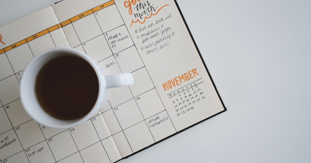 Handwritten monthly calendar with goal notes and a coffee cup — a physical companion to a digital day tracker